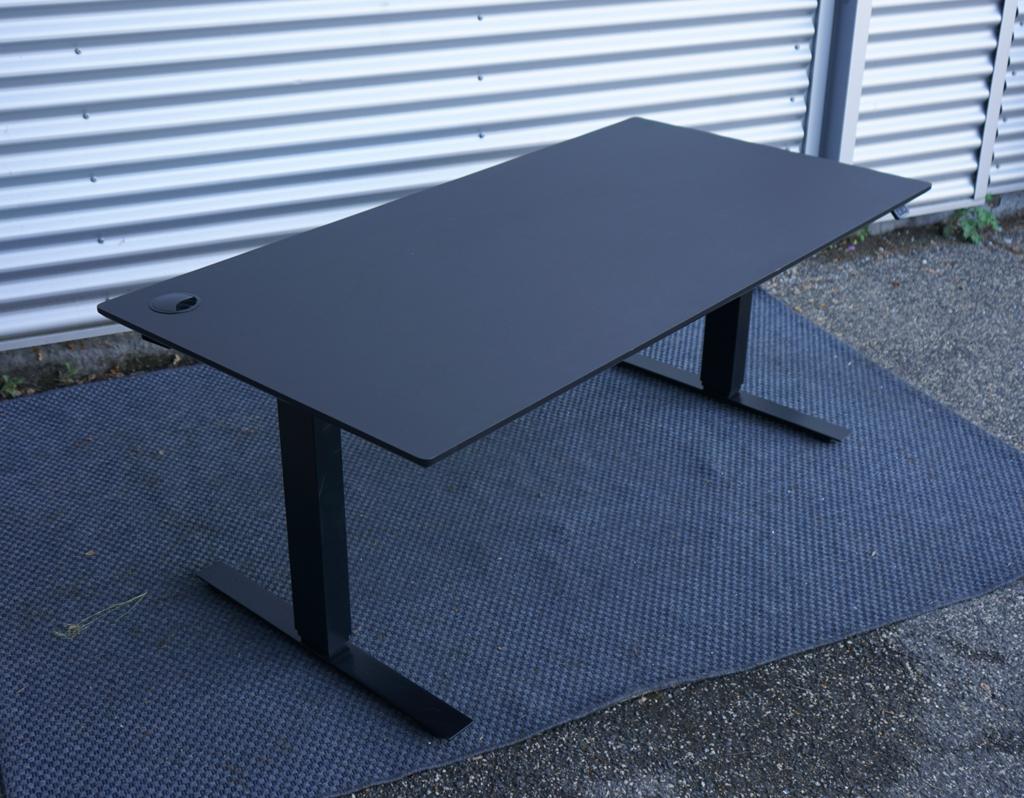 Martela hæve-sænkebord 160x80 cm i sort linoleum med kabelgennemføring og kabelbakke, set fra skrå vinkel.